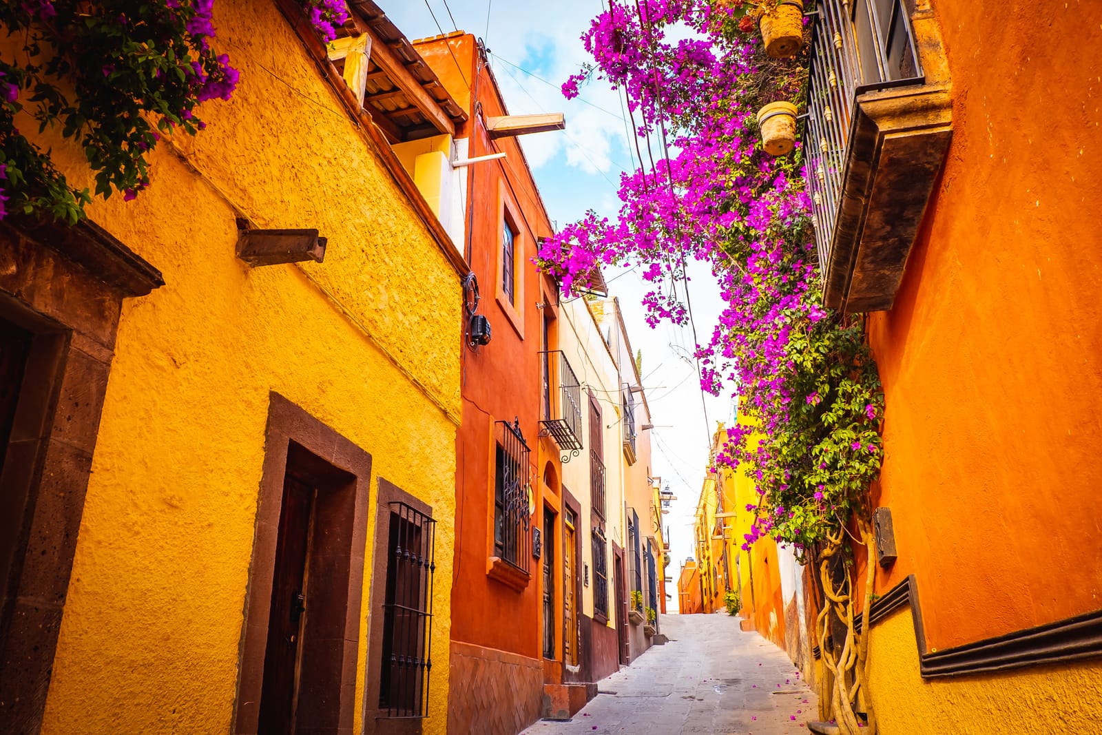 Narrow ochre and orange street draped with bougainvillea