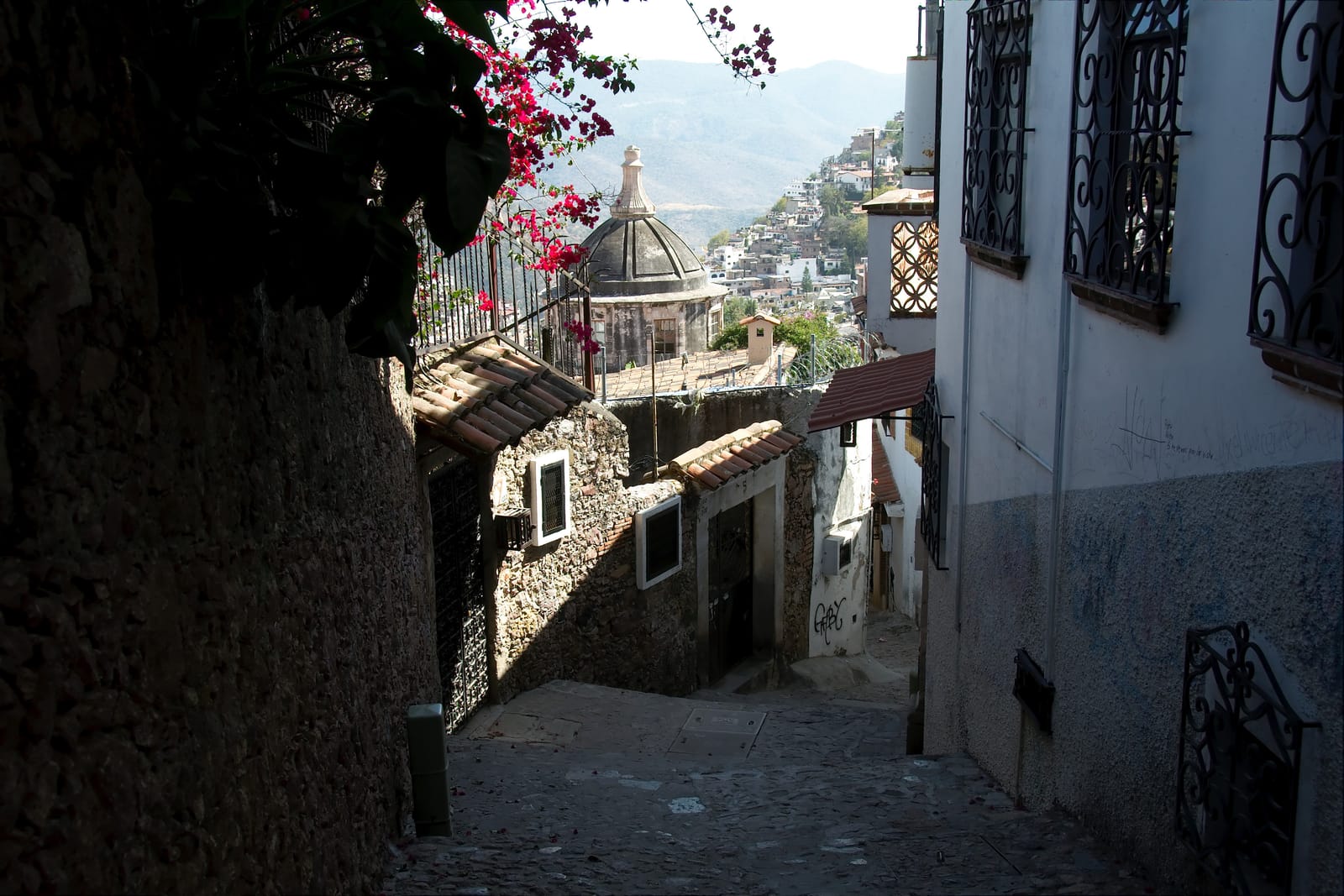 Narrow stone alley with bougainvillea and hillside houses in Taxco